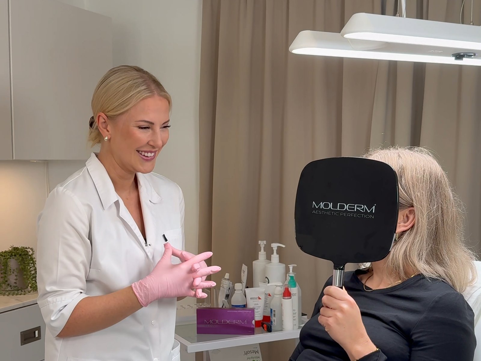 Hanna Axelsson ler bredvid en kund som tittar i en spegel med Molderm-logga på The Lovely Studio